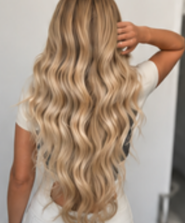 Long, hand-tied blonde extensions with soft waves, seen from behind